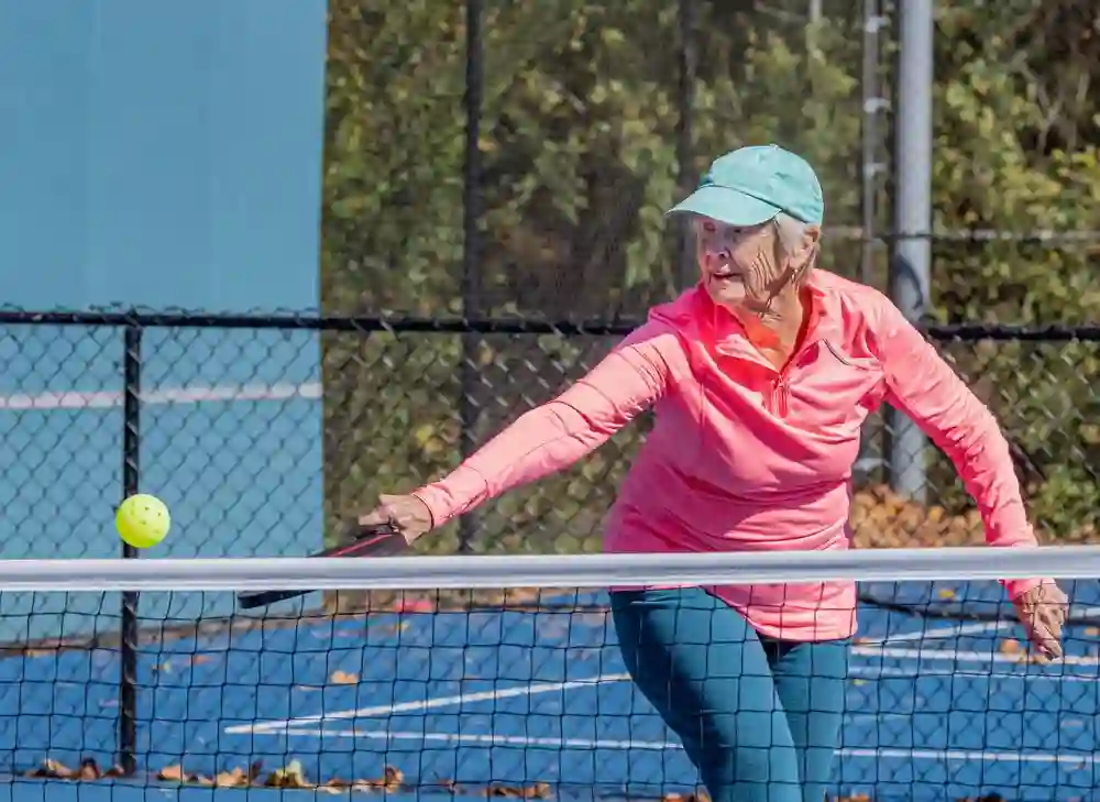 Senior woman reaching to hit pickleball with paddle