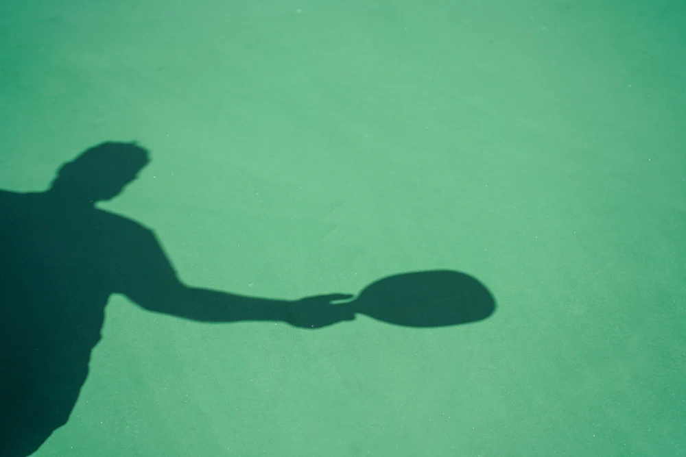 shadow of single pickleball player on green court